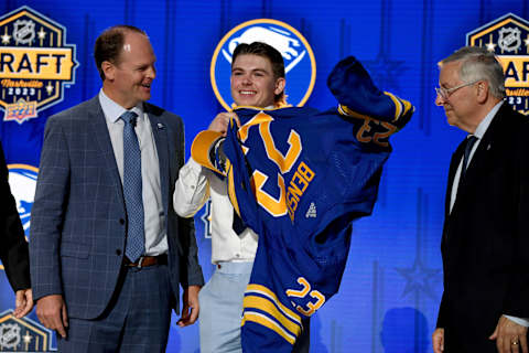 Jun 28, 2023; Nashville, Tennessee, USA; Buffalo Sabres draft pick Zach Benson puts on his sweater after being selected with the thirteenth pick in round one of the 2023 NHL Draft at Bridgestone Arena. Mandatory Credit: Christopher Hanewinckel-USA TODAY Sports