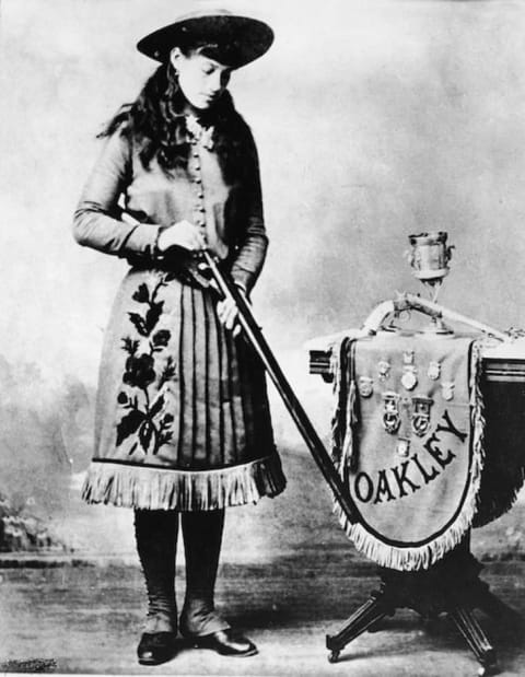 A publicity still of Annie Oakley loading a shotgun.