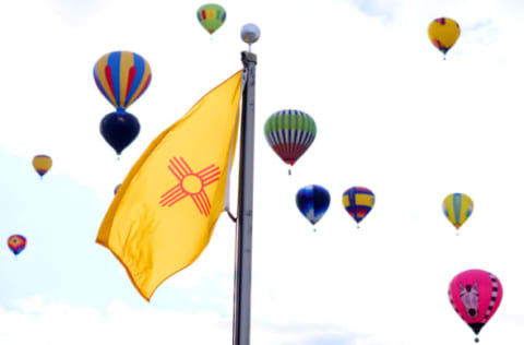 ALBUQUERQUE, NM – OCTOBER 9: Balloons fly past the New Mexico state flag during the 2018 Albuquerque International Balloon Fiesta on October 9, 2018 in Albuquerque, New Mexico. The Albuquerque Balloon Fiesta is the largest hot air balloon festival, drawing more than 500 balloons from all over the world. (Photo by Maddie Meyer/Getty Images for Lumix)