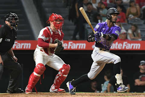 Jul 28, 2021; Anaheim, California, USA; Colorado Rockies left fielder Raimel Tapia (15) hits a single as Los Angeles Angels catcher Max Stassi (middle) looks on during the eighth inning at Angel Stadium. Mandatory Credit: Richard Mackson-USA TODAY Sports