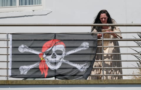 WHITBY, ENGLAND – JULY 06: A woman attaches a Jolly Roger pirate flag to the railings of a pub during the first day of the Whitby Captain Cook Festival on 6 July, 2018 in Whitby, England. The 3-day festival marks the 250th anniversary of James Cook’s first voyage aboard HM Bark Endeavour to the then-unchartered Southern Seas, today New Zealand and Australia. Captain Cook was born in Marton near Middlesbrough and moved to Whitby as an apprentice with a shipping firm. Later he joined the Royal Navy rising through the ratings to become a Captain. His famous ship HM Bark Endeavour was built in Whitby. (Photo by Ian Forsyth/Getty Images)