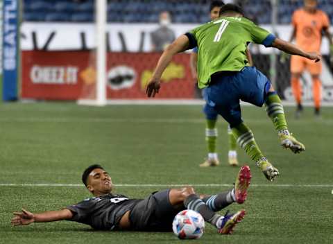 SEATTLE, WASHINGTON – APRIL 16: Cristian Roldan #7 of Seattle Sounders FC leaps over Emanuel Reynoso. (Photo by Steve Dykes/Getty Images)