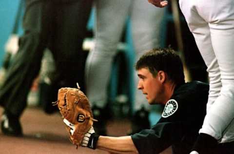 SEATTLE, UNITED STATES: Amidst a sea of his teammates’ legs, Seattle Mariner catcher Dan Wilson displays the Barry Bonds foul ball he caught while sliding onto the step of the Seattle dugout during third inning play against the San Francisco Giants in Seattle WA, 11 June 1999. Seattle went on to win, 7-3. AFP PHOTO Dan Levine (Photo credit should read DAN LEVINE/AFP via Getty Images)