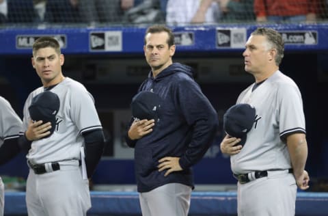 TORONTO, ON - MARCH 30: Quality control coach Carlos Mendoza #64 of the New York Yankees and manager Aaron Boone #17 and third base coach Phil Nevin #53 stand for the playing of the American anthem before the start of their MLB game against the Toronto Blue Jays at Rogers Centre on March 30, 2018 in Toronto, Canada. (Photo by Tom Szczerbowski/Getty Images) *** Local Caption *** Carlos Mendoza;Aaron Boone;Phil Nevin