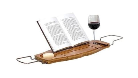 An open book, a wine glass, and a bar of soap on a bathtub caddy