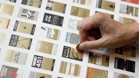 A hand scratching off one of the novels on the scratch-off poster